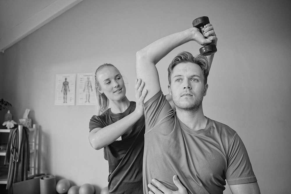 Young physiotherapist helping man exercise with dumbbells